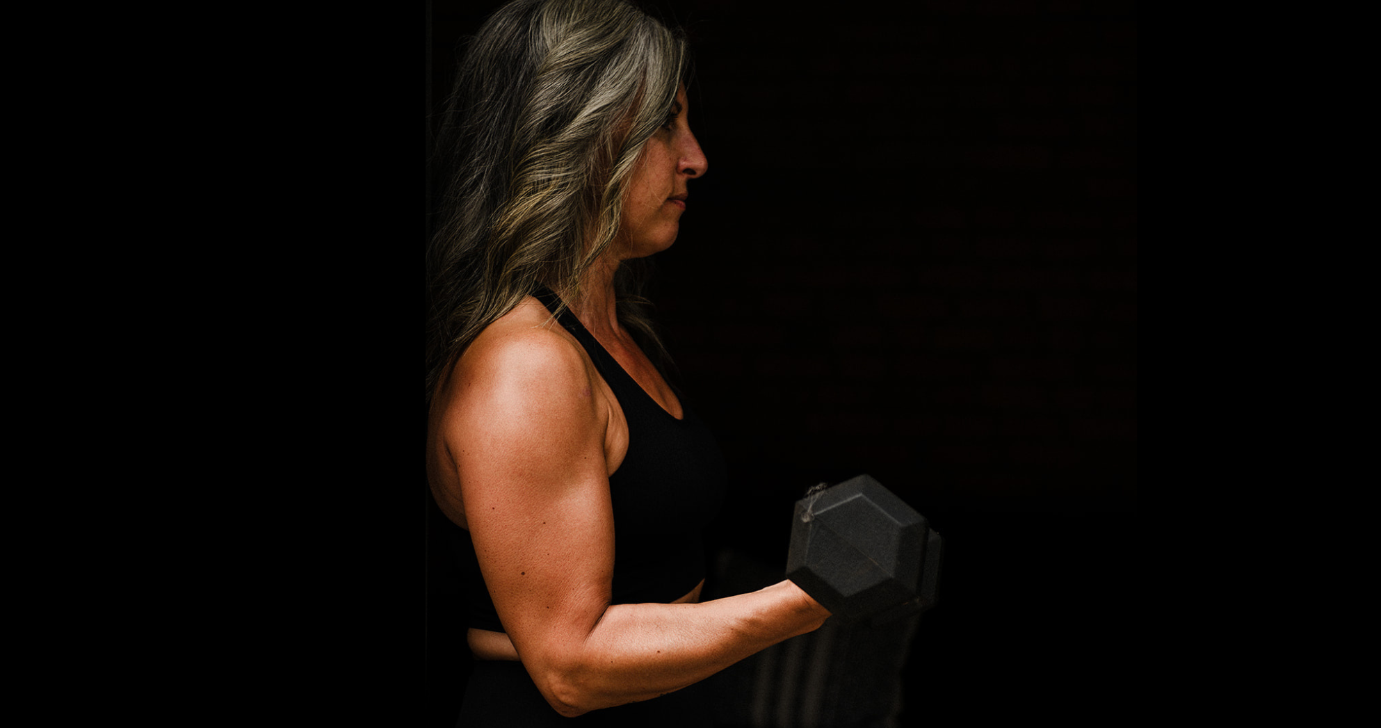 Strong woman performing a bicep curl on a black background to represent the benefits of strength training for your body.