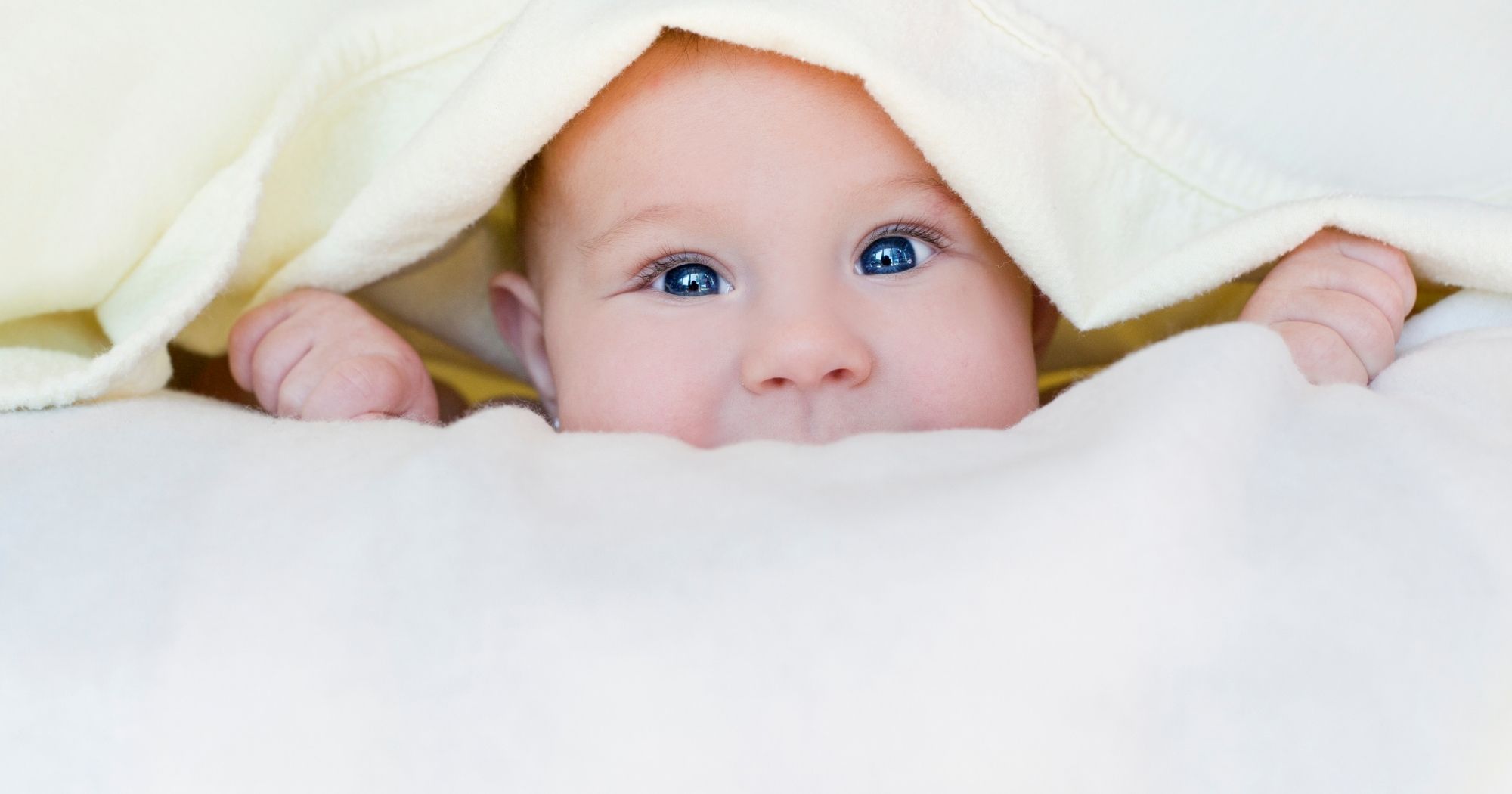 Smiling baby peeking out from blankets during early development